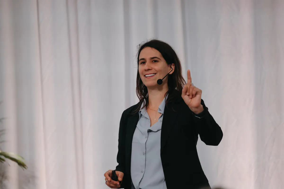 Dr. Ariana Fontenot delivering a keynote on a professional stage, headset mic, mid-gesture.